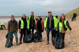 Six people participating in a beach clean holing black bags and wearing high visibility clothing 