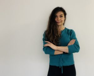 women standing looking at the camera with her arms crossed and a blank wall behind her